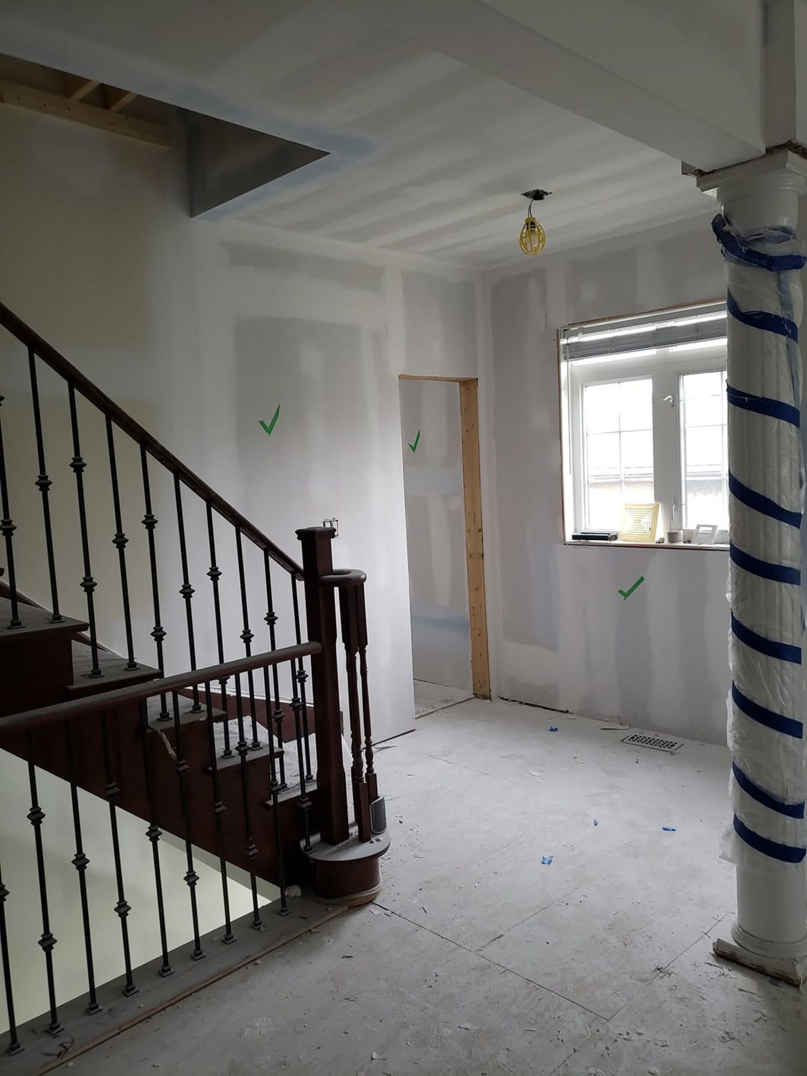 Same interior after drywall installation — walls hung, mudded and taped, green paint-check marks visible on the finished surface.